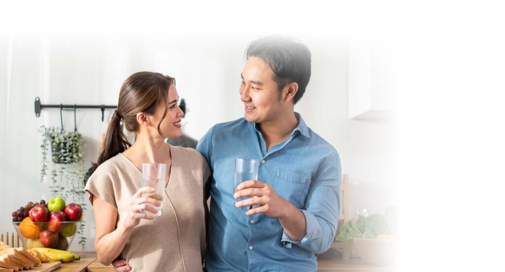 Asian attractive couple drinking a glass of water in kitchen at home. Young thirsty man and woman holding clean mineral natural in cup after waking up and sip in morning for health care in house.